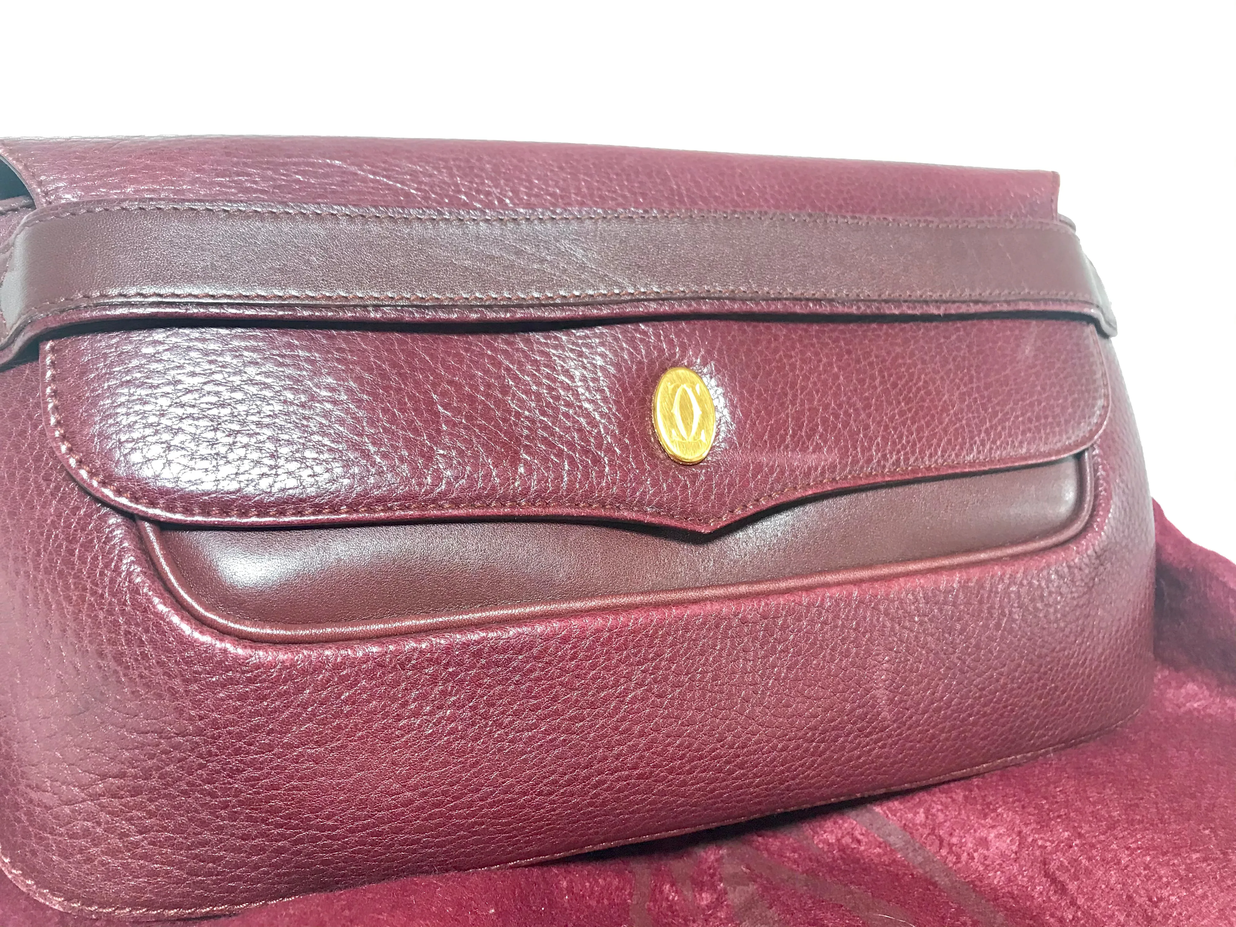 Vintage Cartier wine leather clutch bag with gold tone logo motif. Classic purse from must de Cartier Collection.
